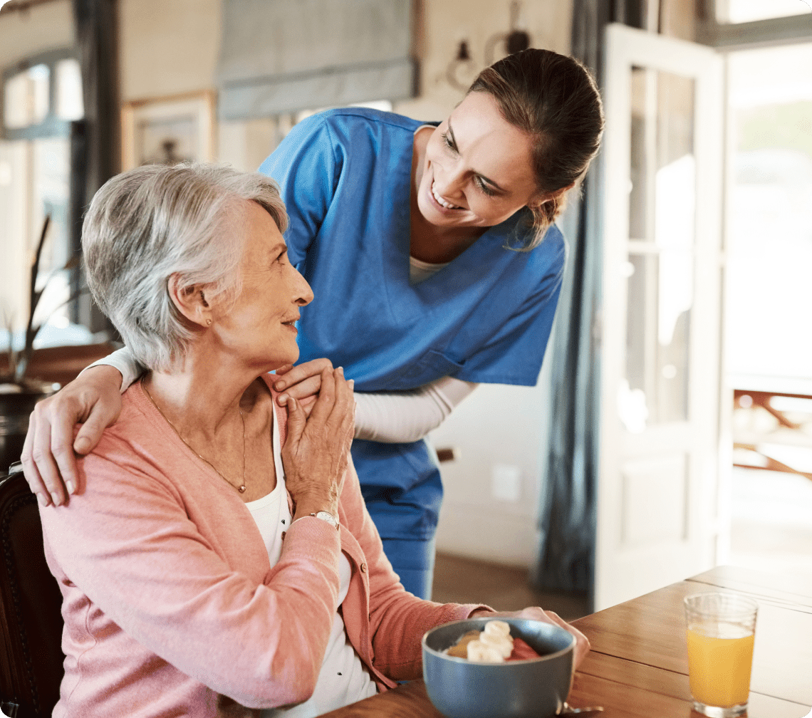 Nurse smiling at elderly woman with breakfast.