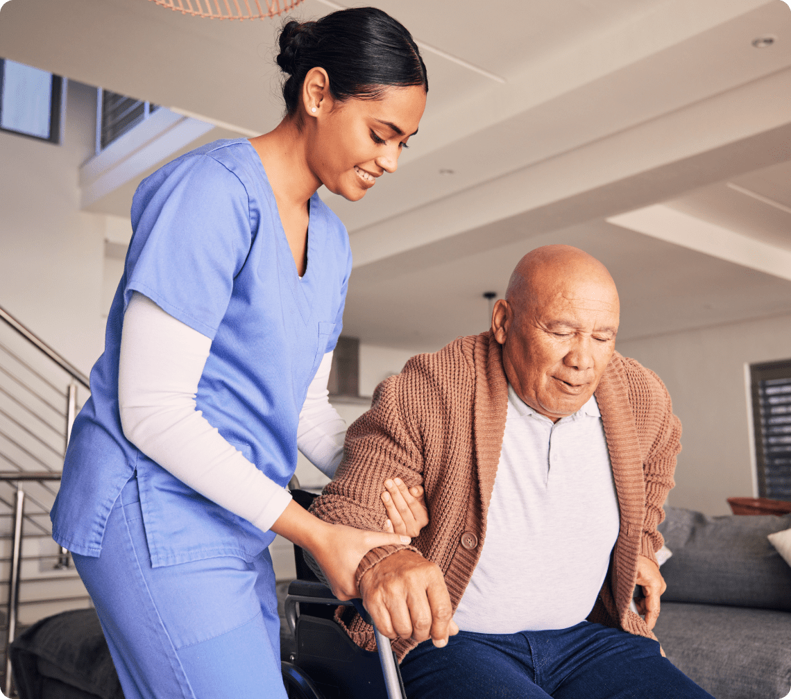 Caregiver assisting elderly man from wheelchair.