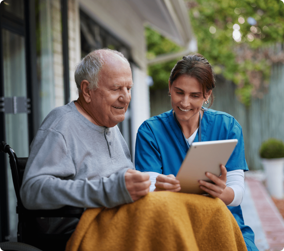Elderly man and caregiver using tablet outside.