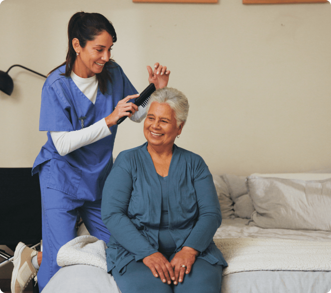 Caregiver combing elderly woman's hair, smiling.