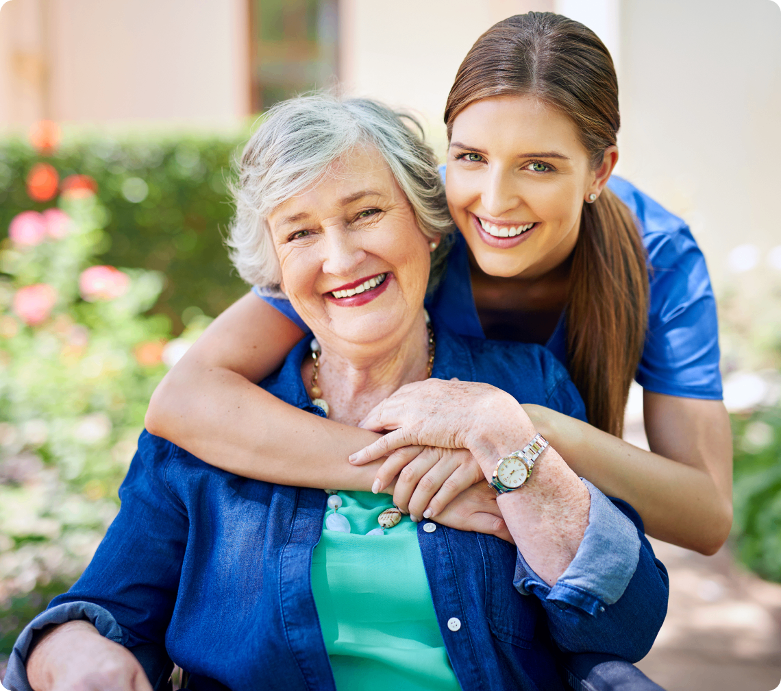 Smiling woman hugging elderly woman outdoors.